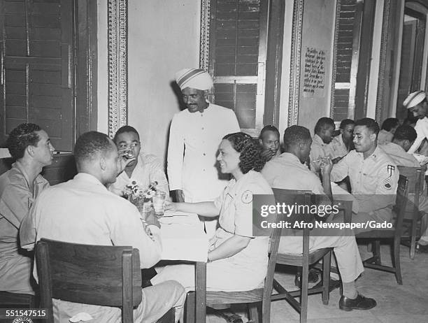 Group of African-American soldiers off duty in World War Two seated with nurses and people in uniform, in the United Services Organization, 1942.