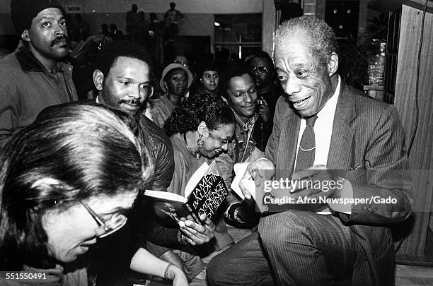 The author James Baldwin sitting and signing books in a crowded book store, 1980.