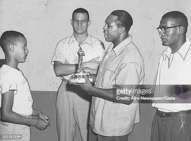 Archie Moore, American professional boxer and the Light Heavyweight World Champion awarding a trophy to a promising young basketball player, 1955.
