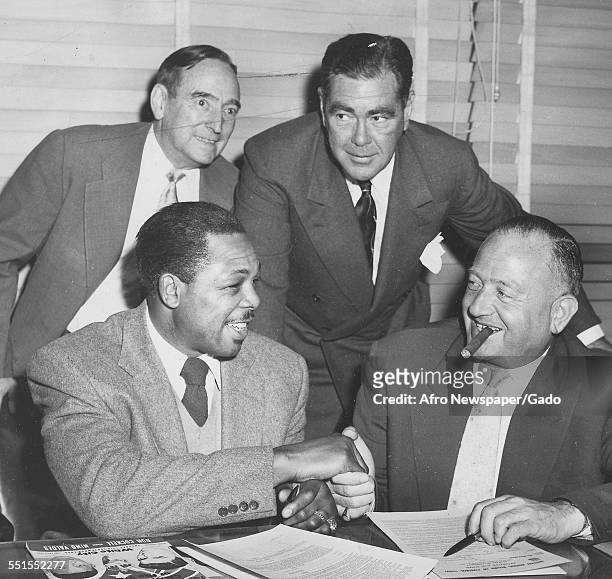 Archie Moore, boxer, signing and shaking on an agreement with Jack Solomon promotor to fight Yoland Pompey from Trinidad, December 11, 1955.