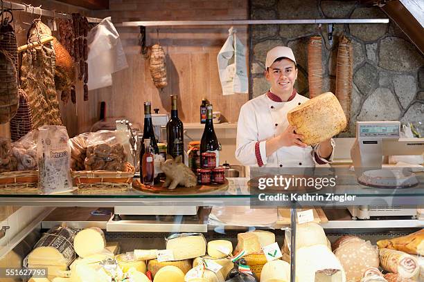 young man working at delicatessen, holding cheese - delicatessen stock pictures, royalty-free photos & images