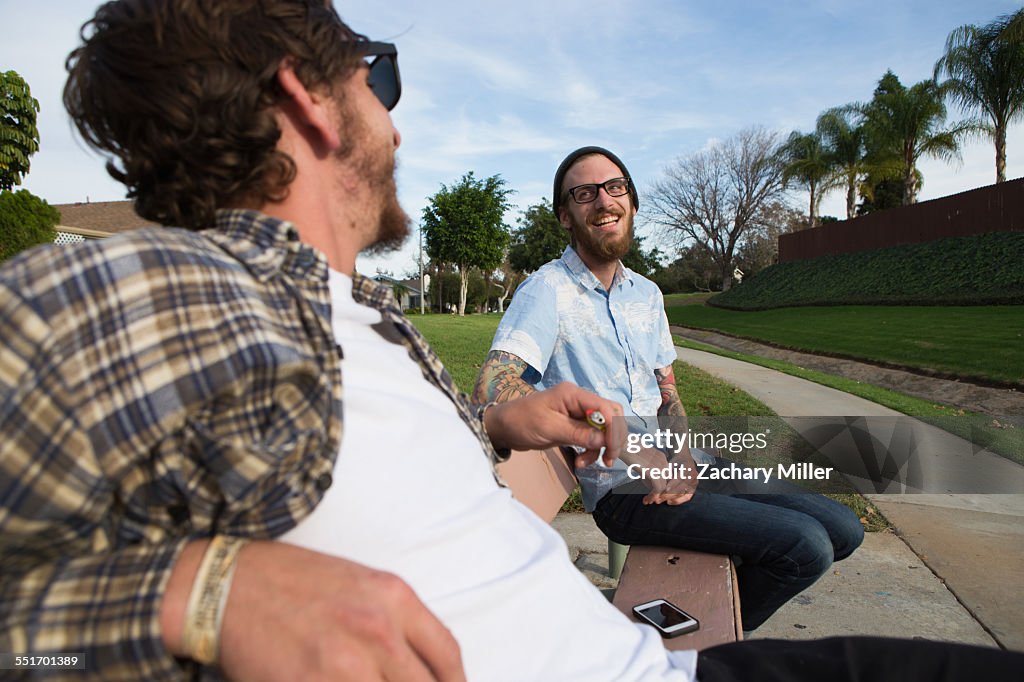 Two young male friends chatting on suburban bench