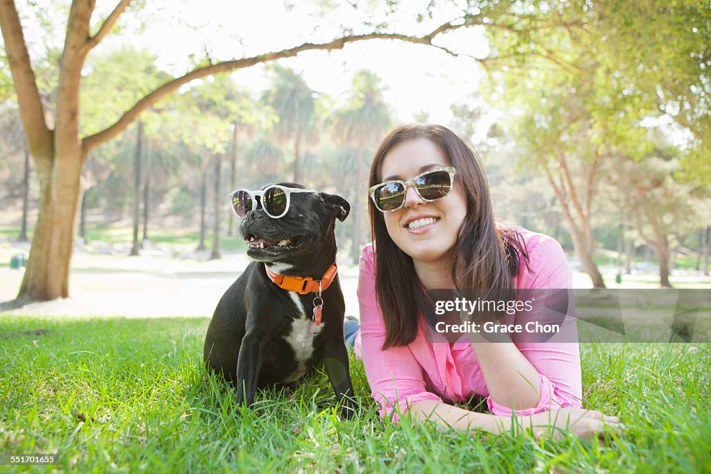 Portrait of young woman and dog lying in park wearing sunglasses