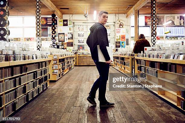 young man holding vinyl record in music store - looking over shoulder photos et images de collection