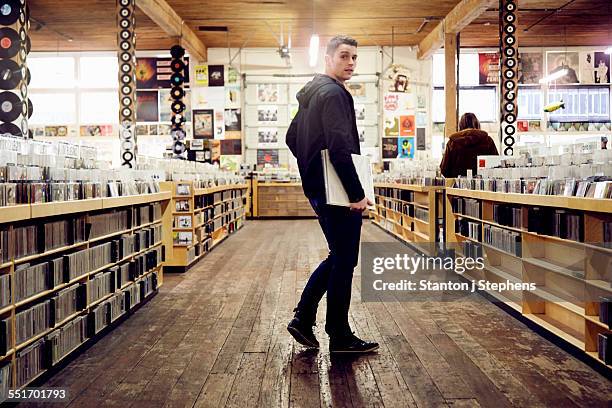 young man holding vinyl record in music store - man looking over shoulder stock pictures, royalty-free photos & images