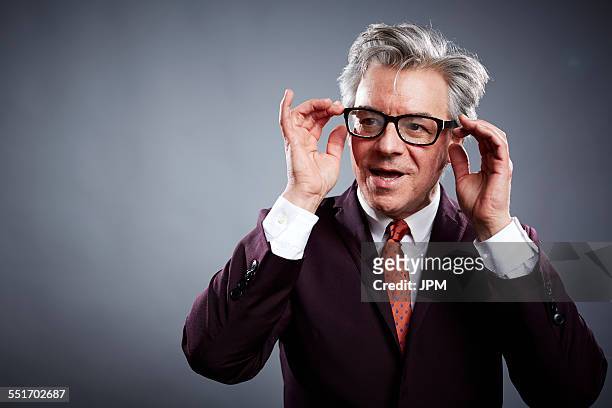 studio portrait of mature businessman adjusting his spectacles - adjusting suit stock pictures, royalty-free photos & images