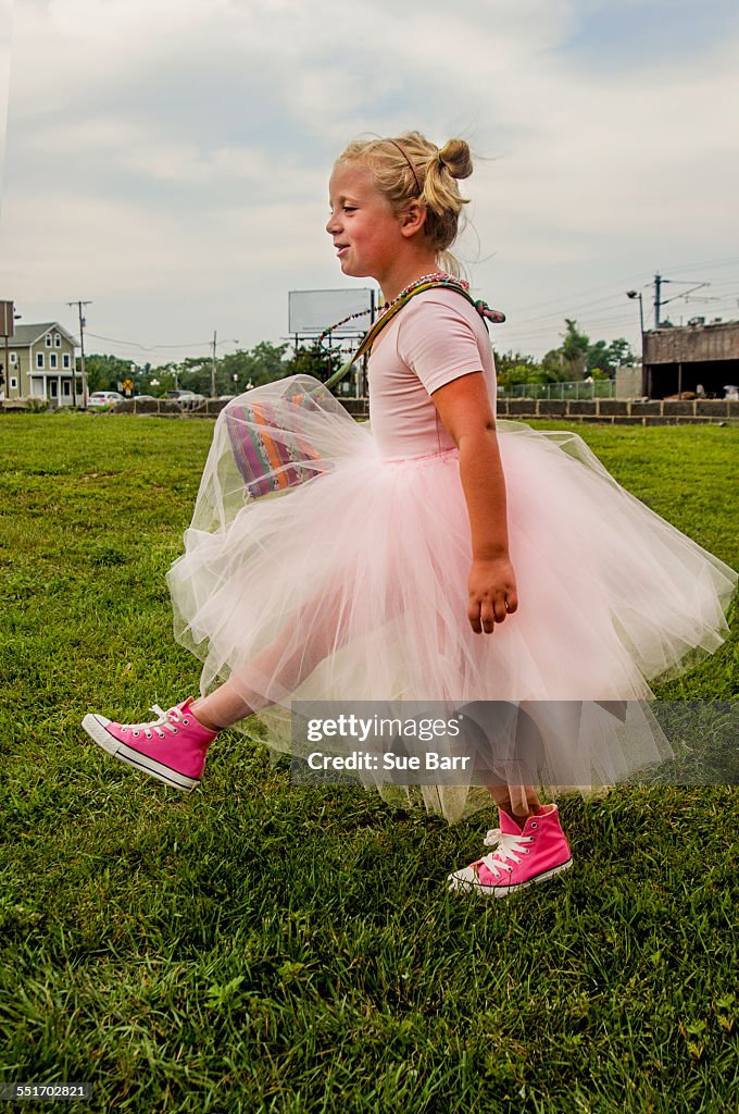 Young girl wearing tutu and pink baseball boots, walking on grass