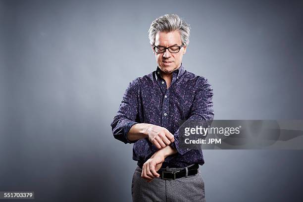 studio portrait of mature businessman rolling up his sleeves - rolling up sleeve stock-fotos und bilder