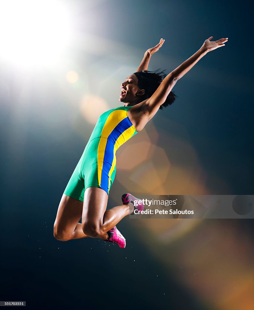 Young female athlete jumping mid air in celebration in stadium