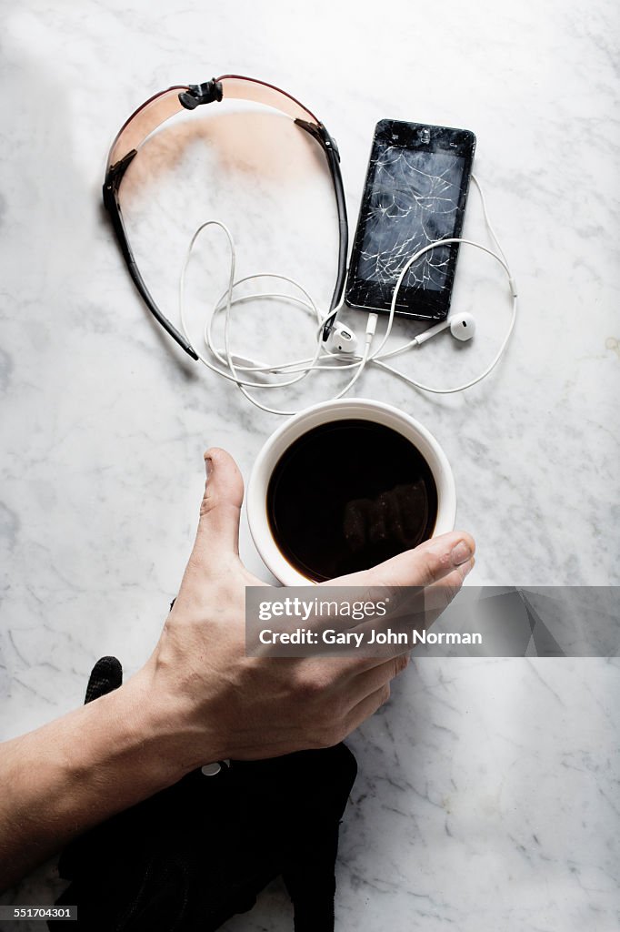 Hand of bike messenger with coffee, glasses, broken smartphone