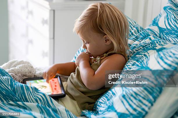female toddler sitting up in bed using digital tablet - thumb sucking stock pictures, royalty-free photos & images