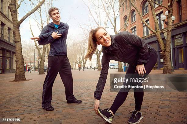 male and female runners warming up on tree lined street, pioneer square, seattle, usa - chándal fotografías e imágenes de stock