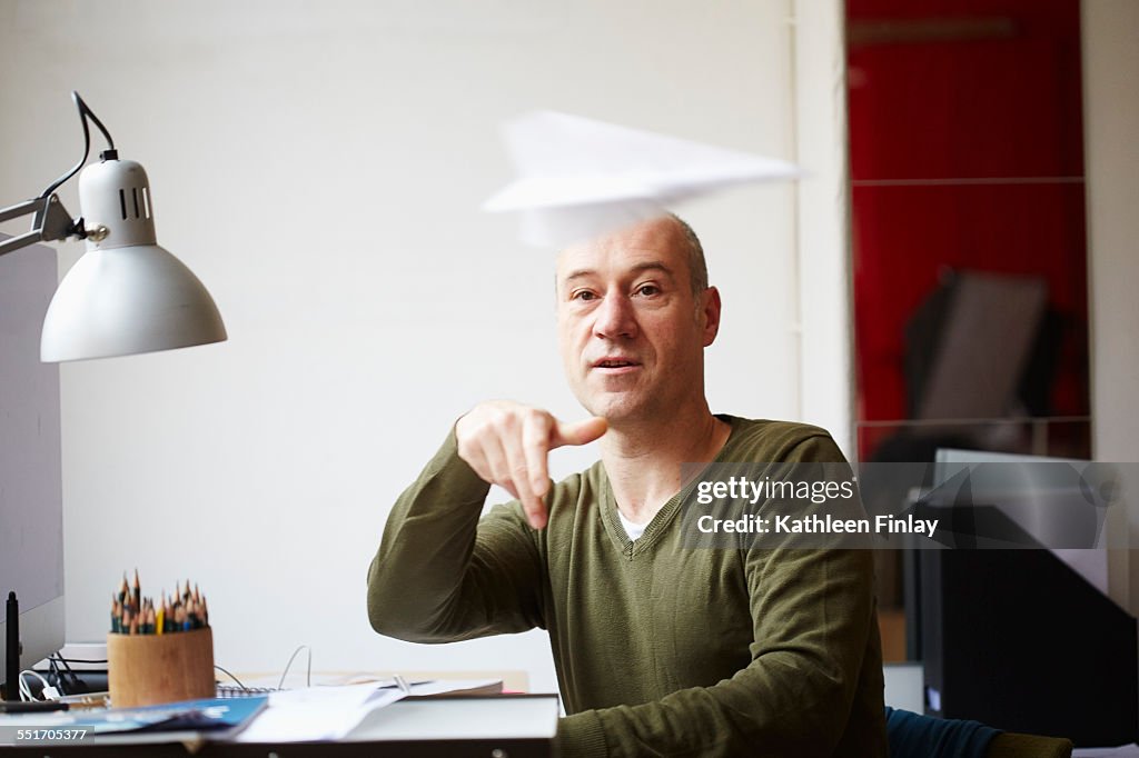Mature man at desk throwing paper airplane