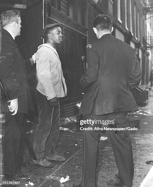 In the aftermath of a riot, police officers, one with a billy club and other with a shotgun, arrest a unidentified man at Franklin and Gilmor...