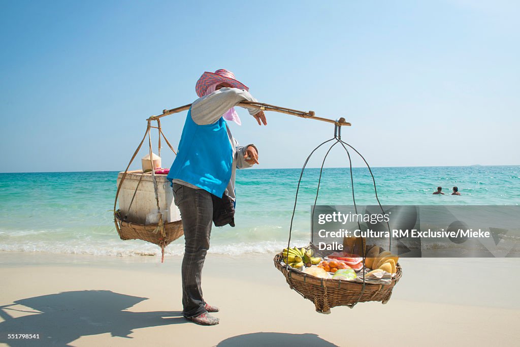 Person carrying traditional baskets of fruit on beach, Koh Samet, Thailand