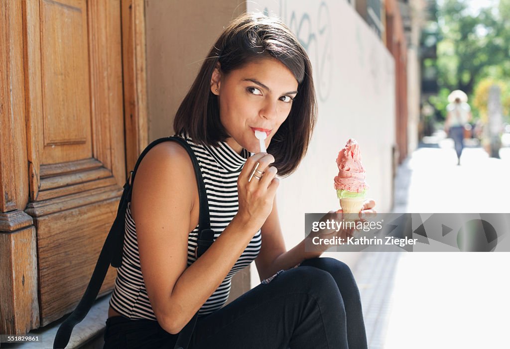 Young woman sitting on doorstep, eating ice cream