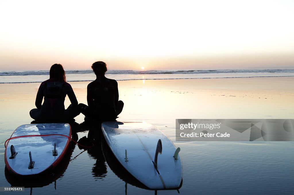 Surfers at sunset , sitting on surfboard