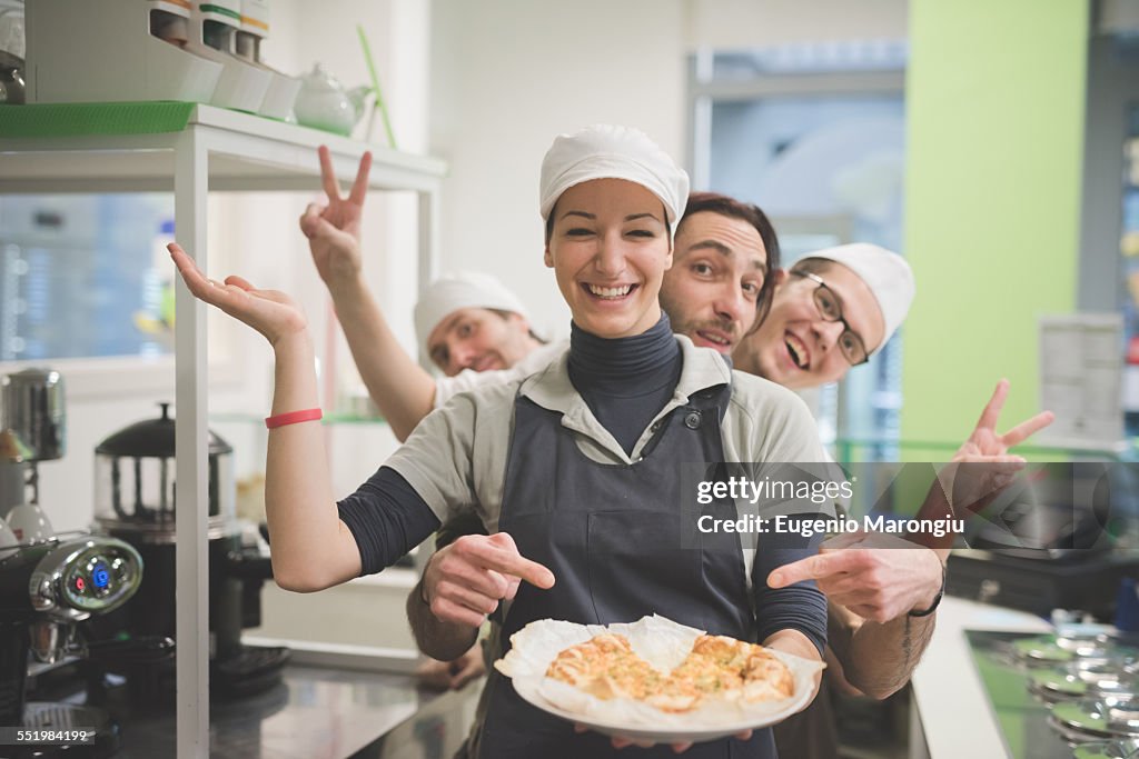 Waitress carrying plate of food, colleagues making fun behind