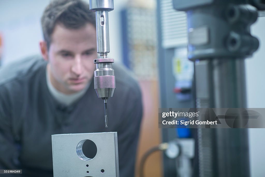 Young male technician checking metal drill machine in workshop