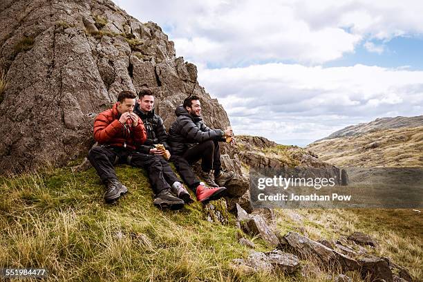 three young male hiking friends eating sandwiches, the lake district, cumbria, uk - outdoor guy sitting on a rock stock pictures, royalty-free photos & images