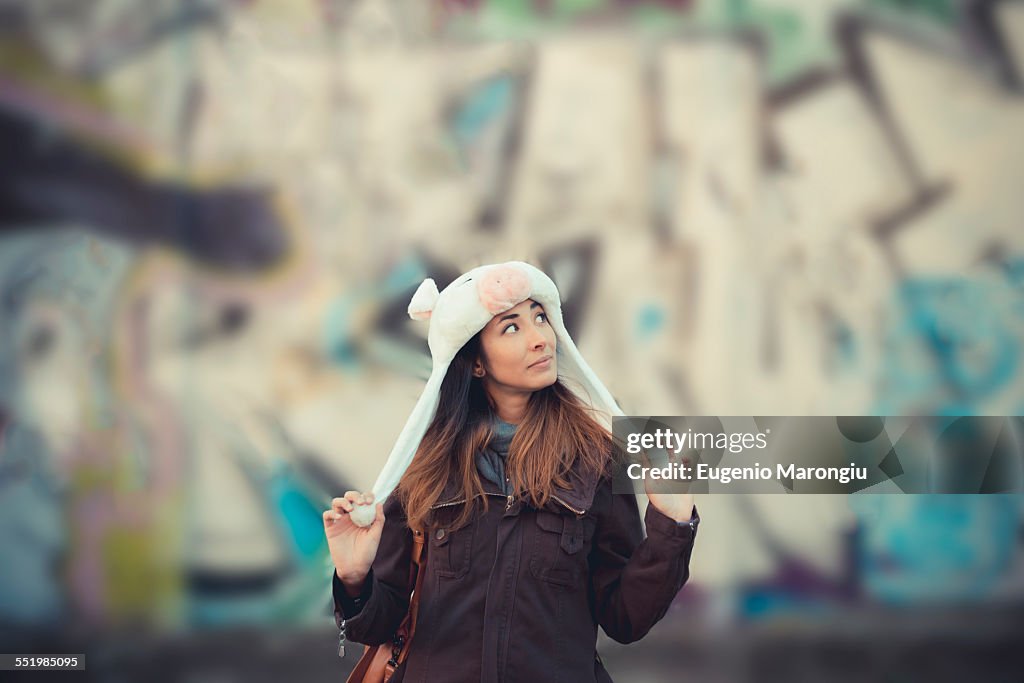 Portrait of mid adult woman wearing fur hat in front of graffiti wall