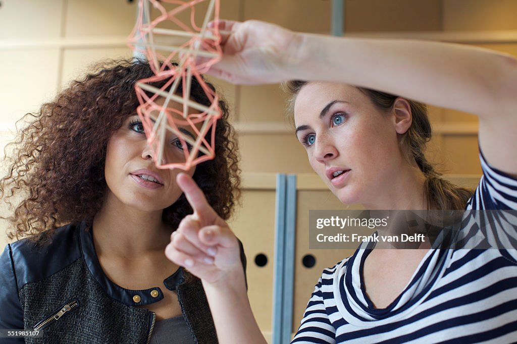 Two young female designers looking at handmade model in creative office