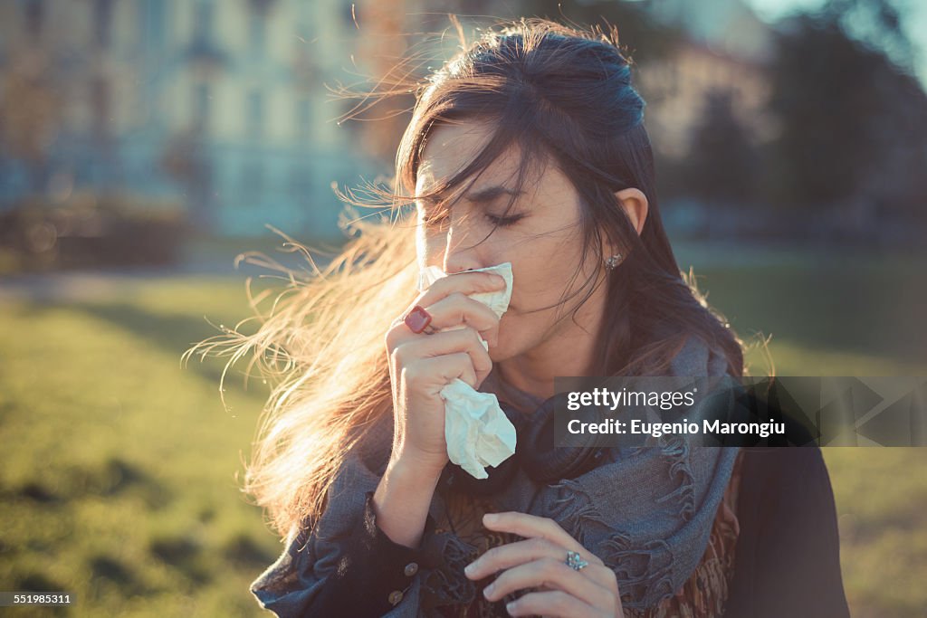 Mid adult woman blowing nose with hankerchief in park