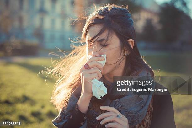 mid adult woman blowing nose with hankerchief in park - blowing nose stock pictures, royalty-free photos & images