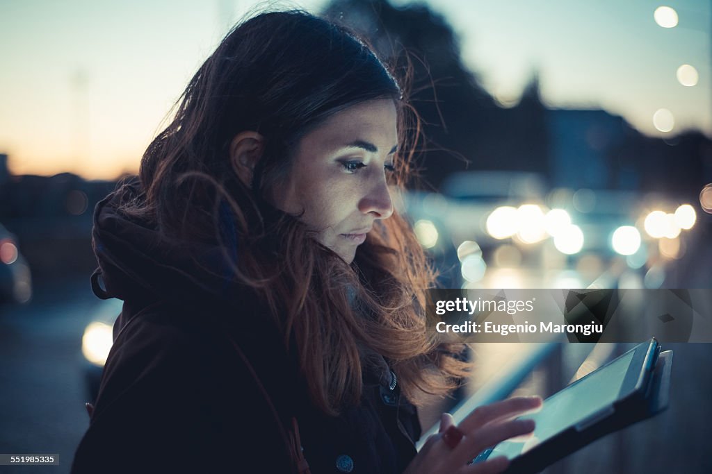 Mid adult woman using digital tablet touchscreen on street at dusk