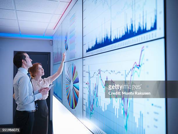 business colleagues studying graphs on screen in meeting room - gegevens stockfoto's en -beelden