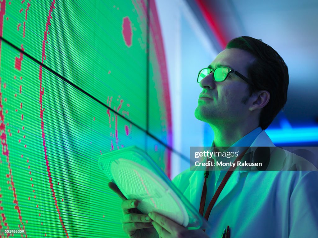 Male scientist with silicon wafer studying graphical display of wafer on screens