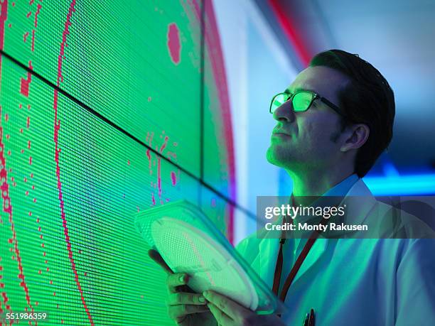male scientist with silicon wafer studying graphical display of wafer on screens - silicone chemische stof stockfoto's en -beelden