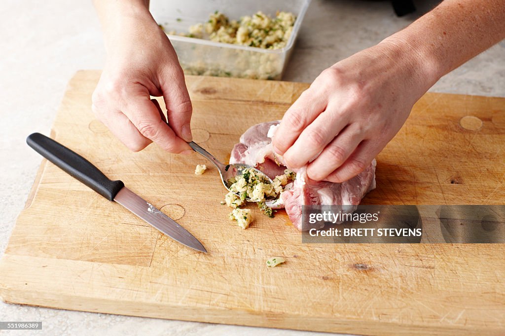 Womans hands stuffing pork steaks on chopping board