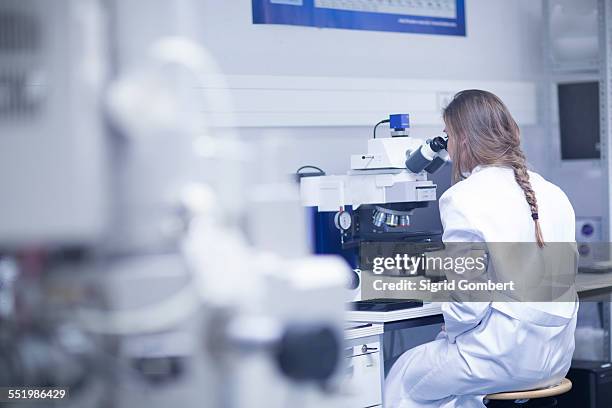 female scientist looking through scanning electron microscope in lab - microscopio electrónico fotografías e imágenes de stock