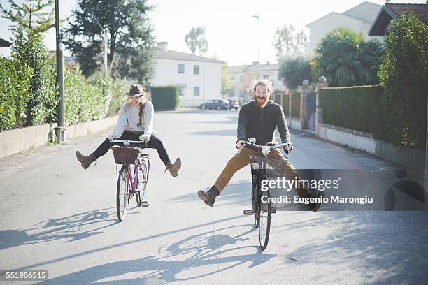 young couple cycling with legs out - fun couple on bike stock-fotos und bilder