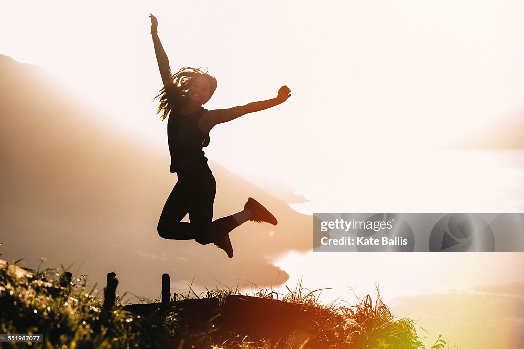 Silhouetted view of young woman jumping mid air at sunset above Lake Atitlan, Guatemala