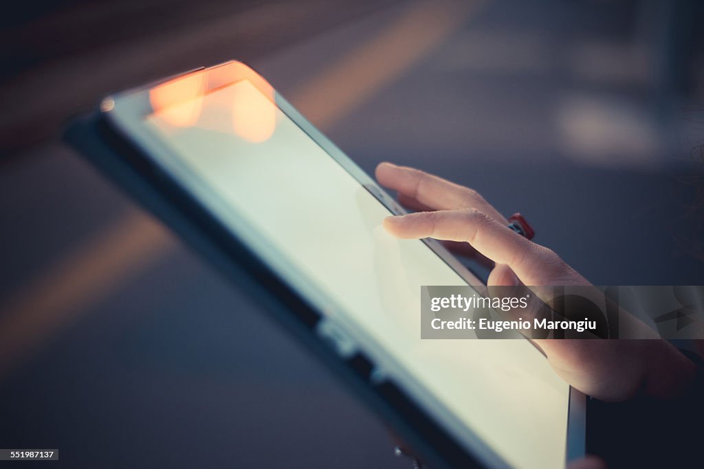 Hand of woman using digital tablet touchscreen at dusk