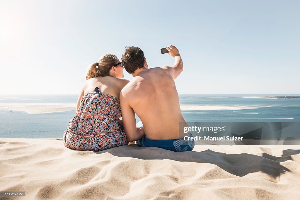 Rear view of young couple taking selfie, Dune de Pilat, France