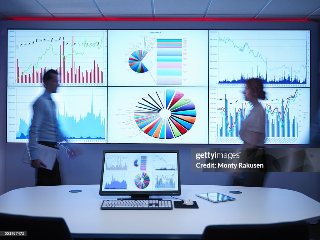 Business people walking in front of graphs on screen