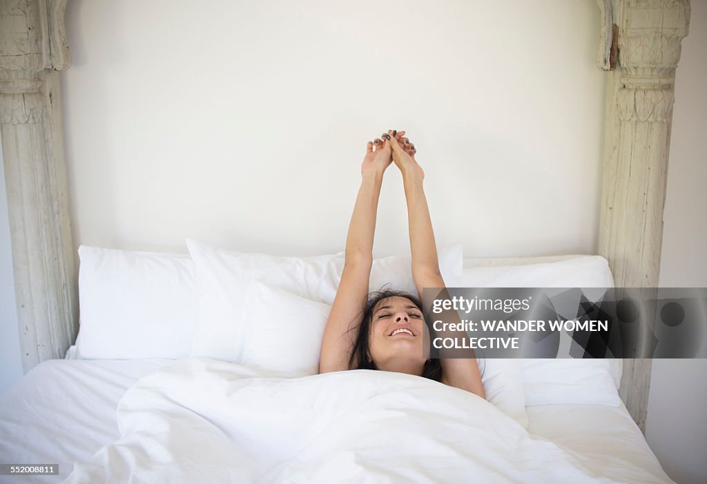 Woman stretching and waking up in bed at home