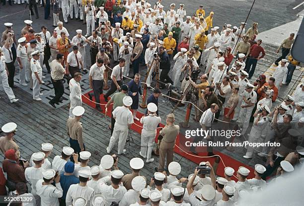 United States astronauts Virgil I 'Gus' Grissom and John Young walk along a red carpet laid out on the deck of the USS Intrepid aircraft carrier...