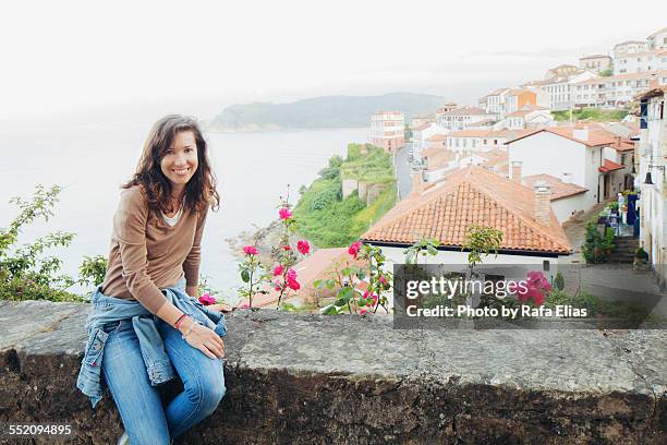 pretty happy woman sitting on wall - lastres village in asturias - fotografias e filmes do acervo