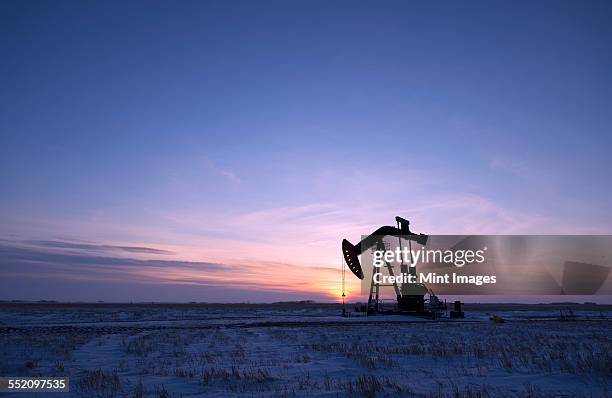 an oil drilling rig and pumpjack on a flat plain in the canadian oil fields at sunset. - piattaforma petrolifera foto e immagini stock