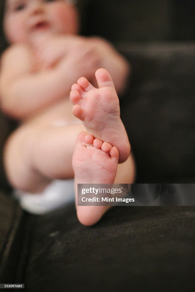 A baby lying on a sofa, wearing a diaper.