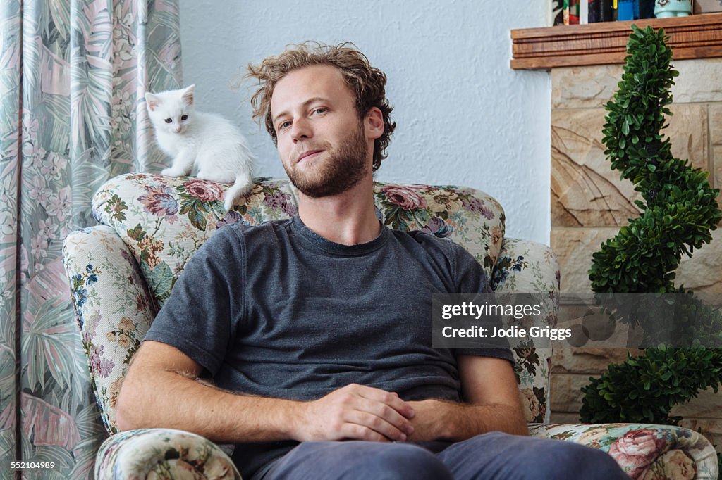 Young man sitting at home with small white kitten