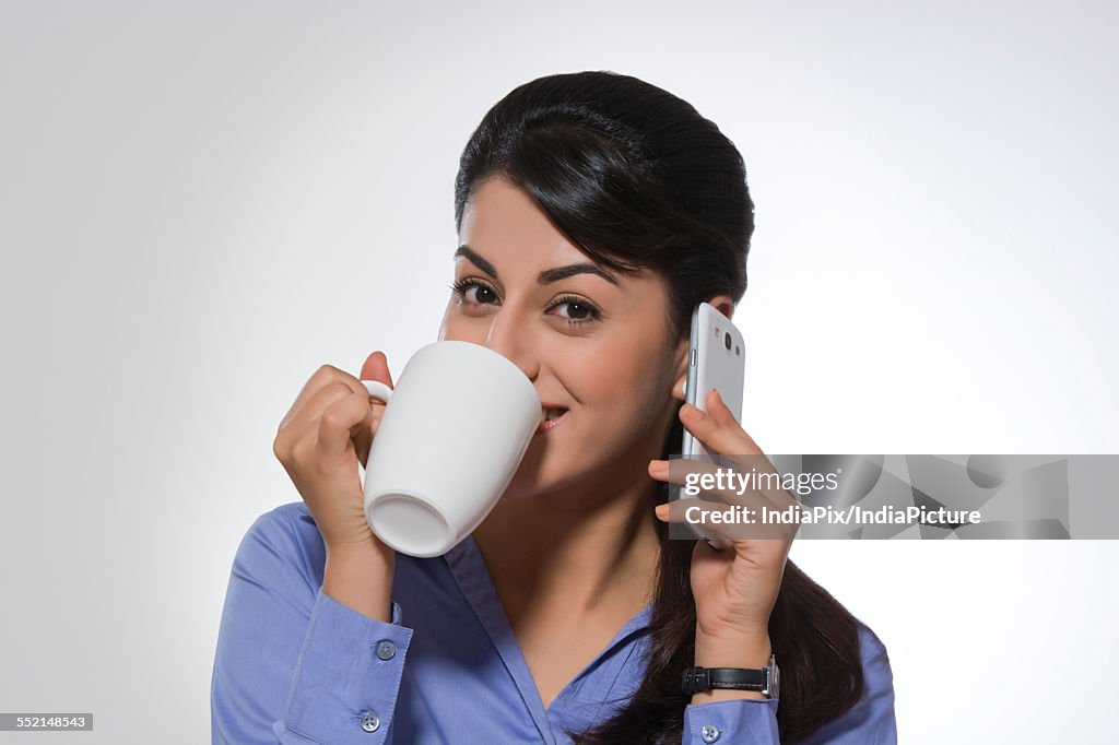 Portrait of beautiful businesswoman using phone while having coffee against gray background