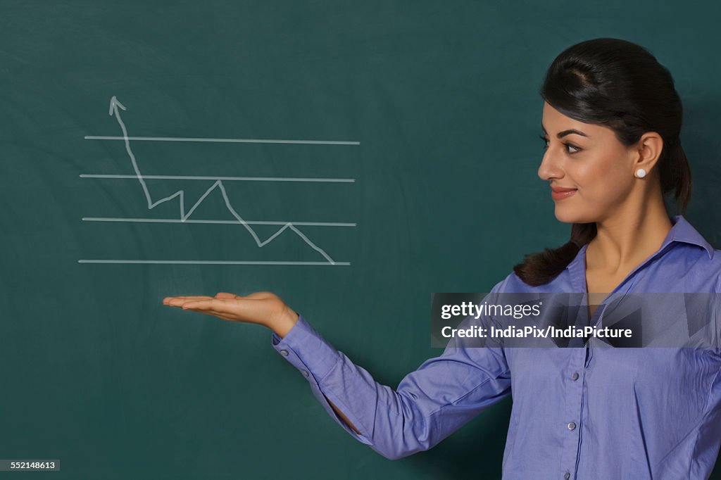 Confident young businesswoman displaying graph on green board at office