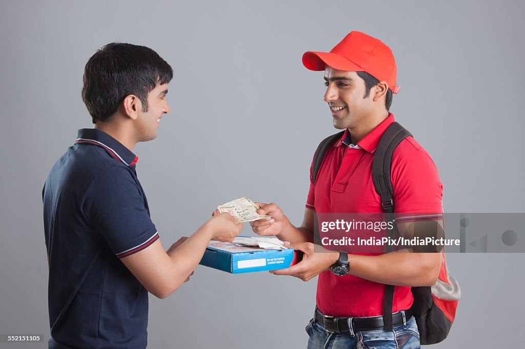 Smiling delivery man delivering pizza to customer against gray background