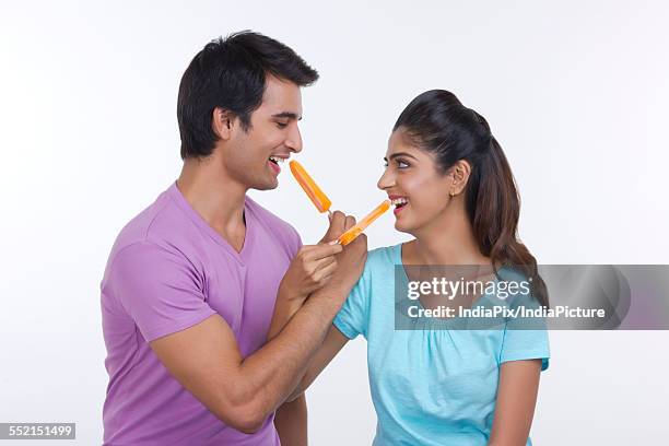 loving young couple feeding each other ice lollies over white background - wassereis mit orangengeschmack stock-fotos und bilder