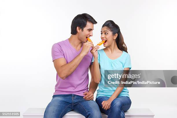 loving young couple eating ice lollies on bench isolated over white background - wassereis mit orangengeschmack stock-fotos und bilder